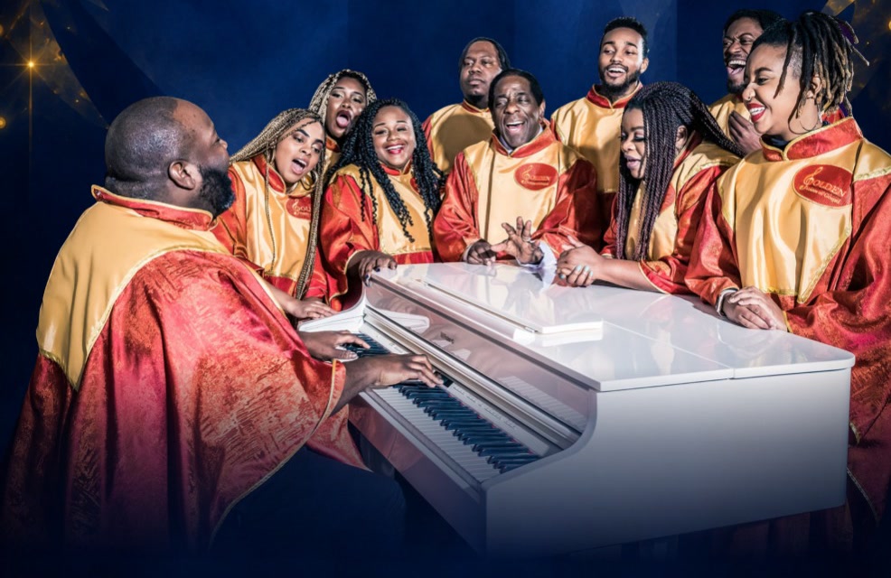 The Golden Voices of Gospel choir in red and gold robes, singing around a white grand piano